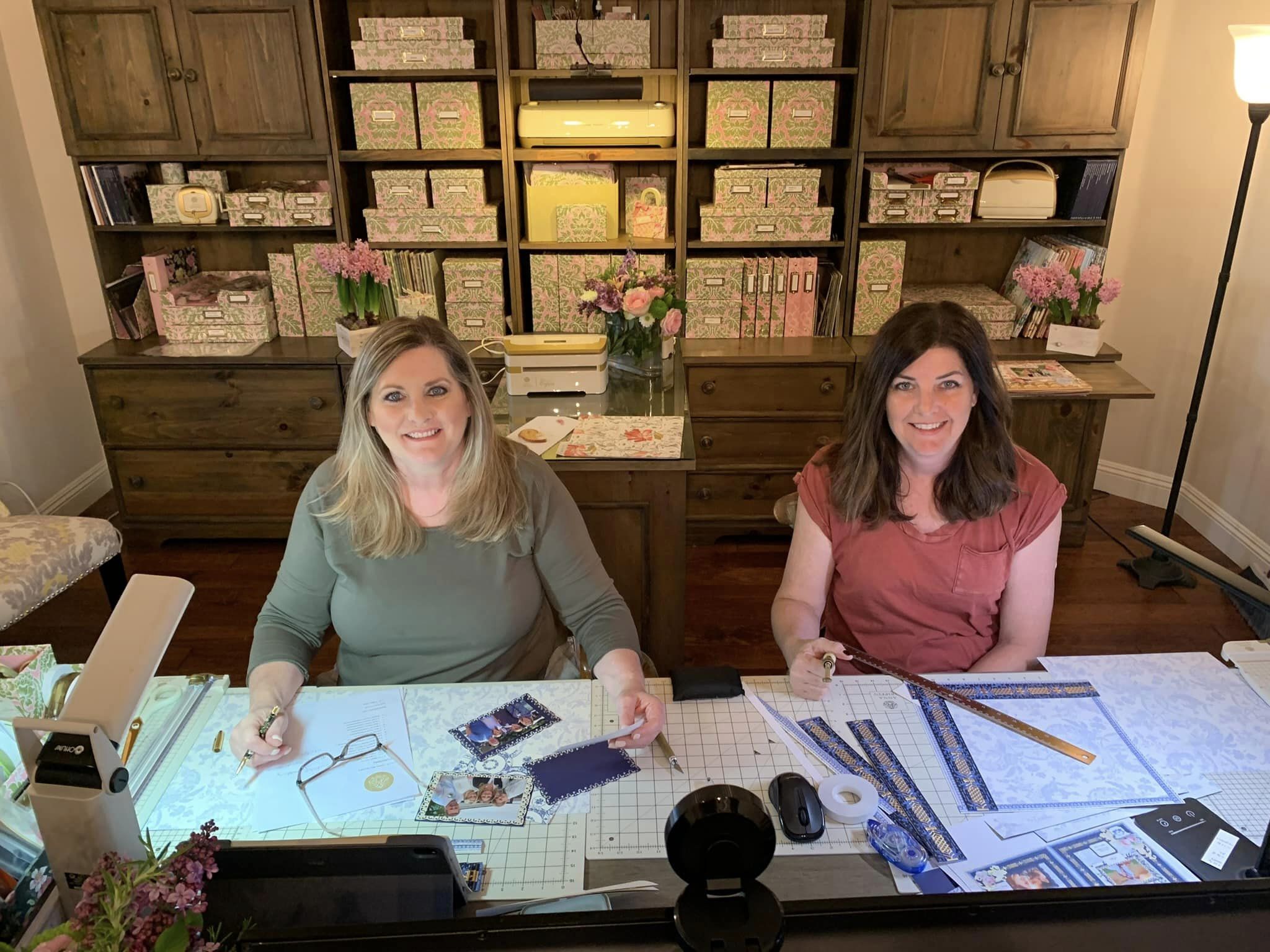 two women sitting at a table working on crafts.