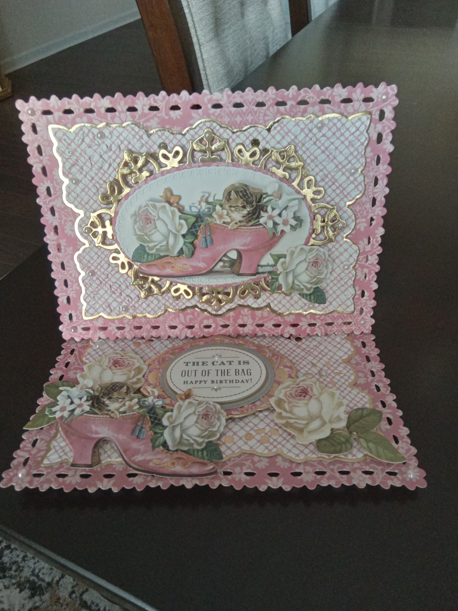 A pink and gold card with a cat and flowers.