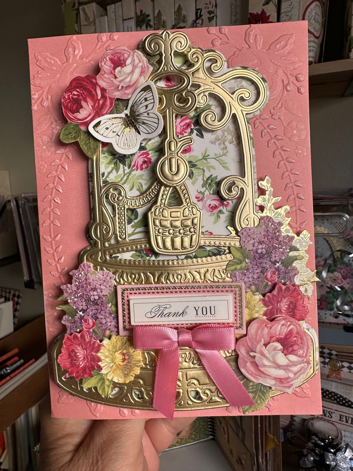 A hand holding a pink card with a bird cage and flowers.