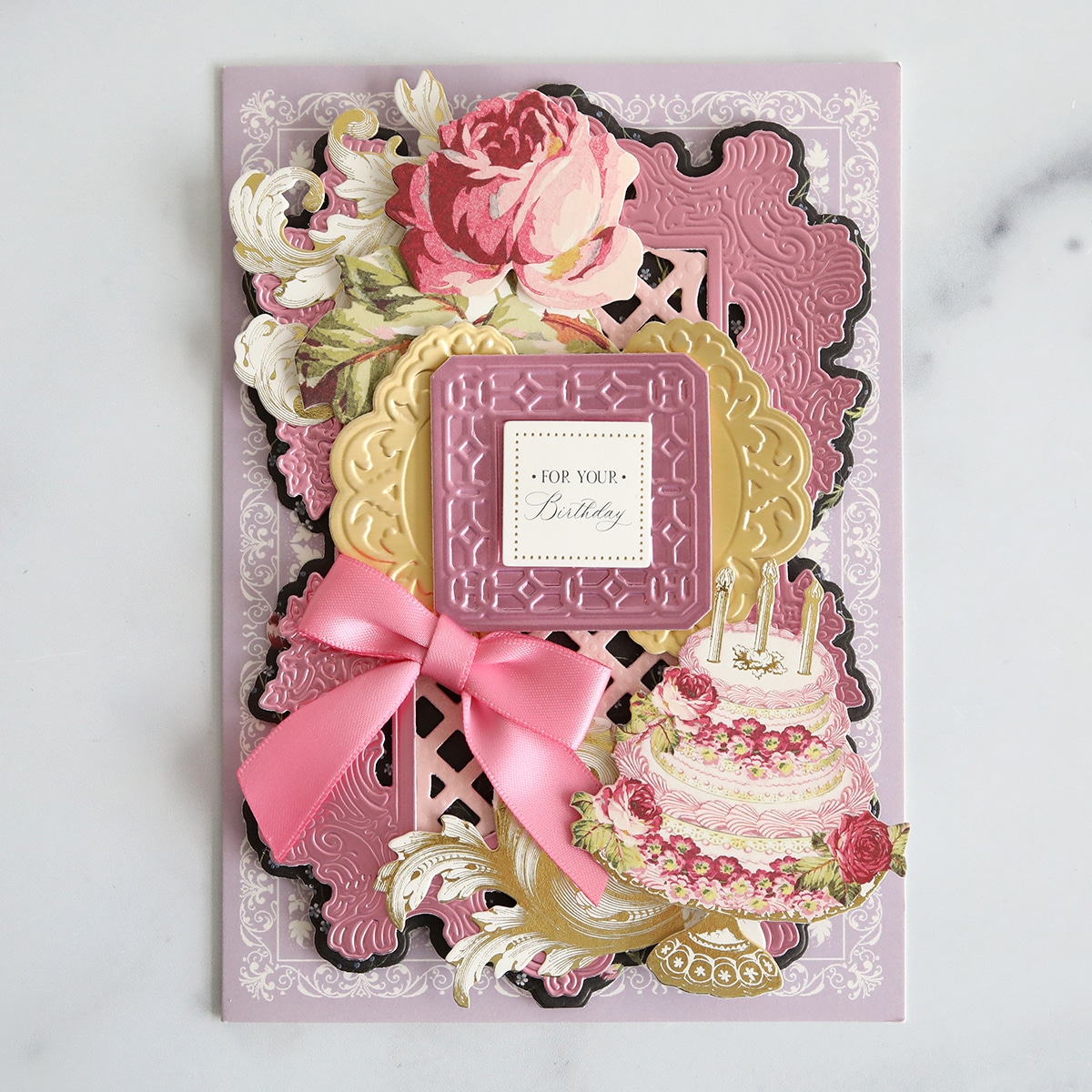 A pink and gold card with flowers and ribbons.