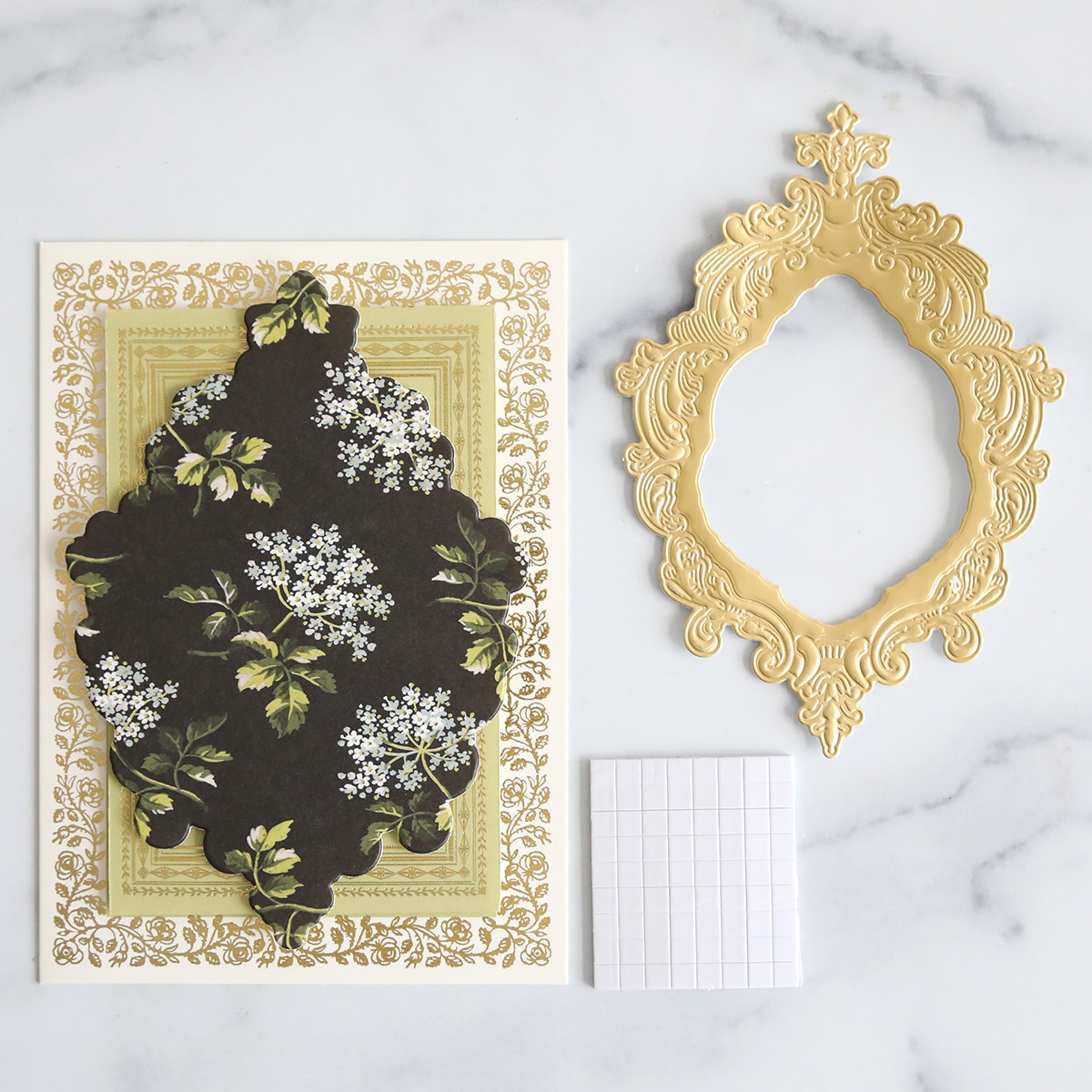 A gold frame with flowers and a notepad on a marble table.