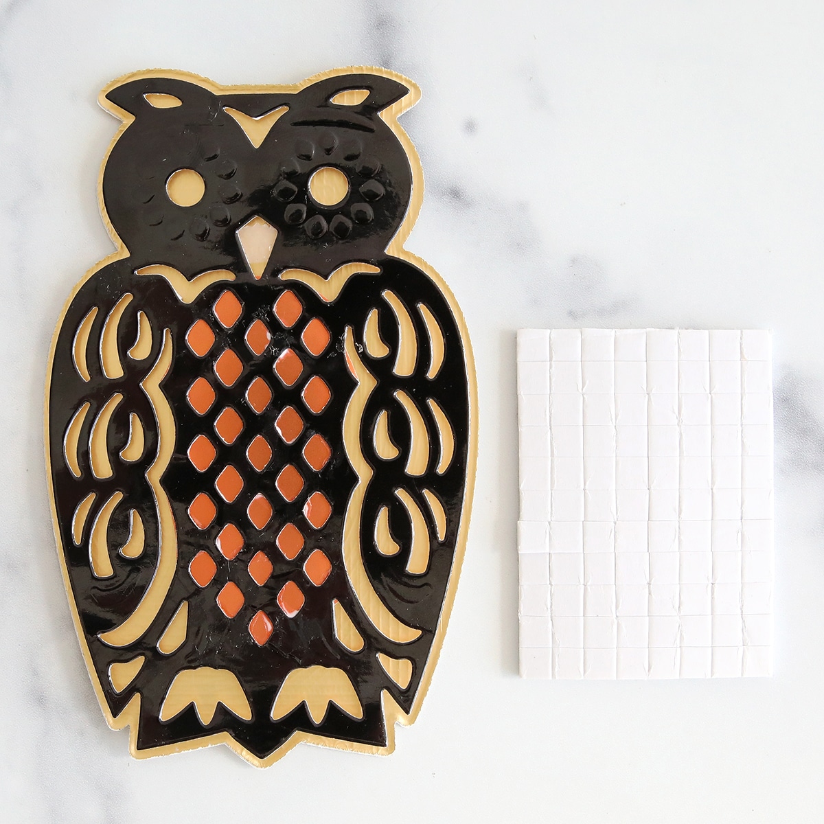 A black and orange owl cookie cutter next to a square of tiles.