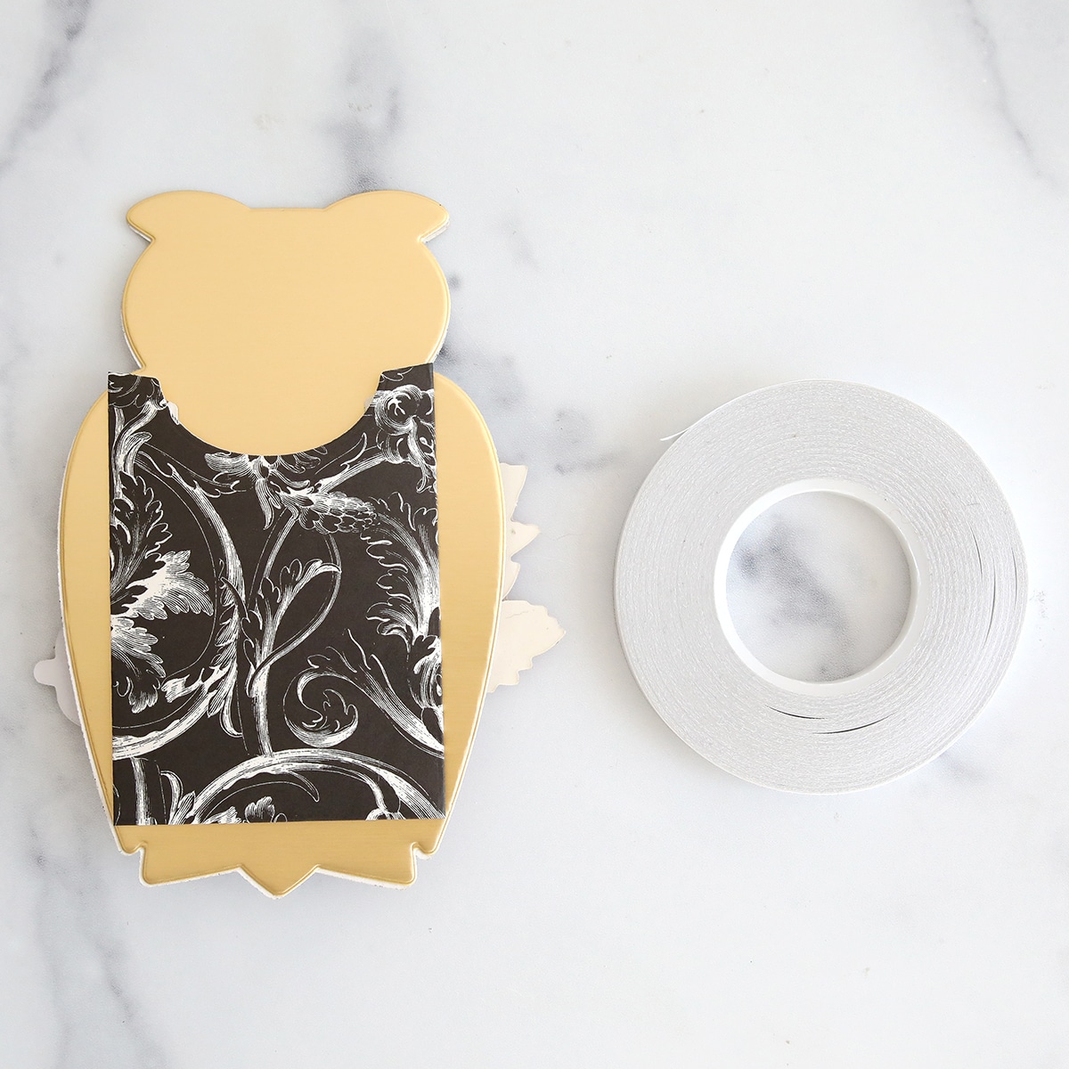 A gold and black owl with tape on a marble table.