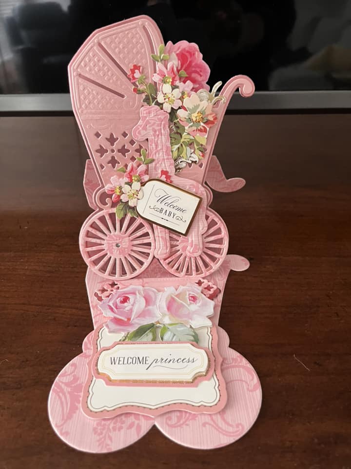 A pink card with a baby carriage and flowers.