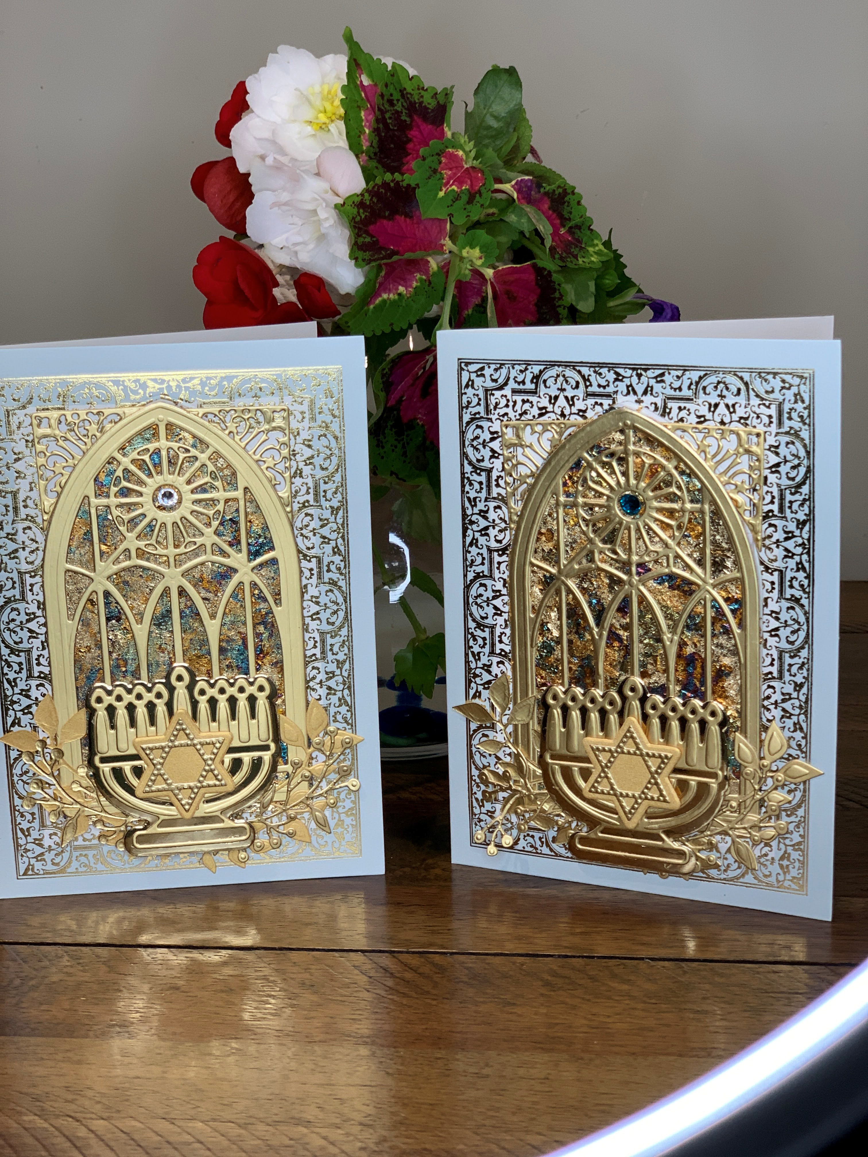 Two hanukkah cards on a table with flowers.