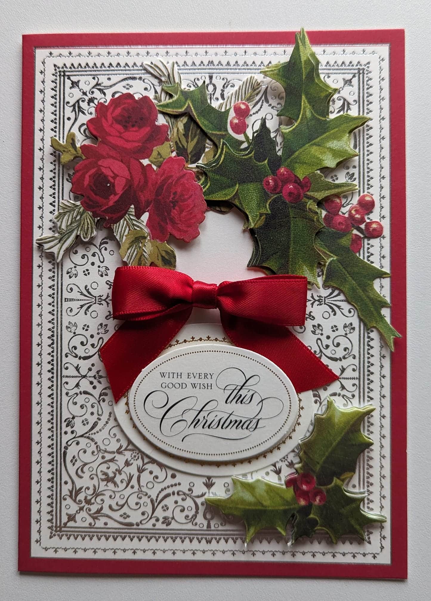 A christmas card with red roses and holly.
