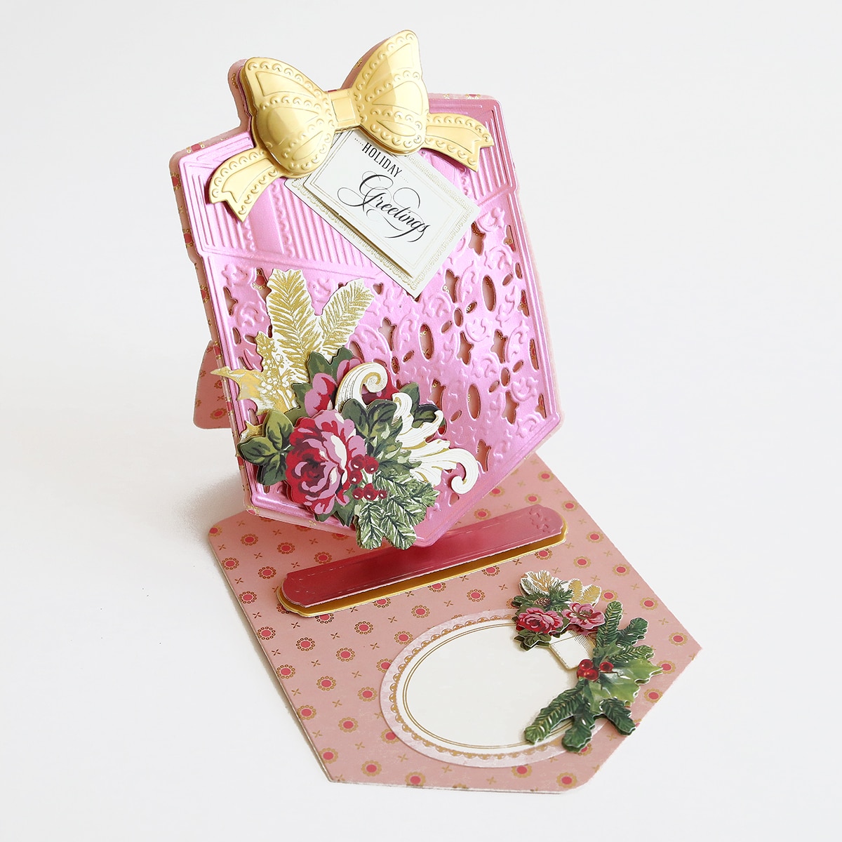 A pink card with holly and bows on it.