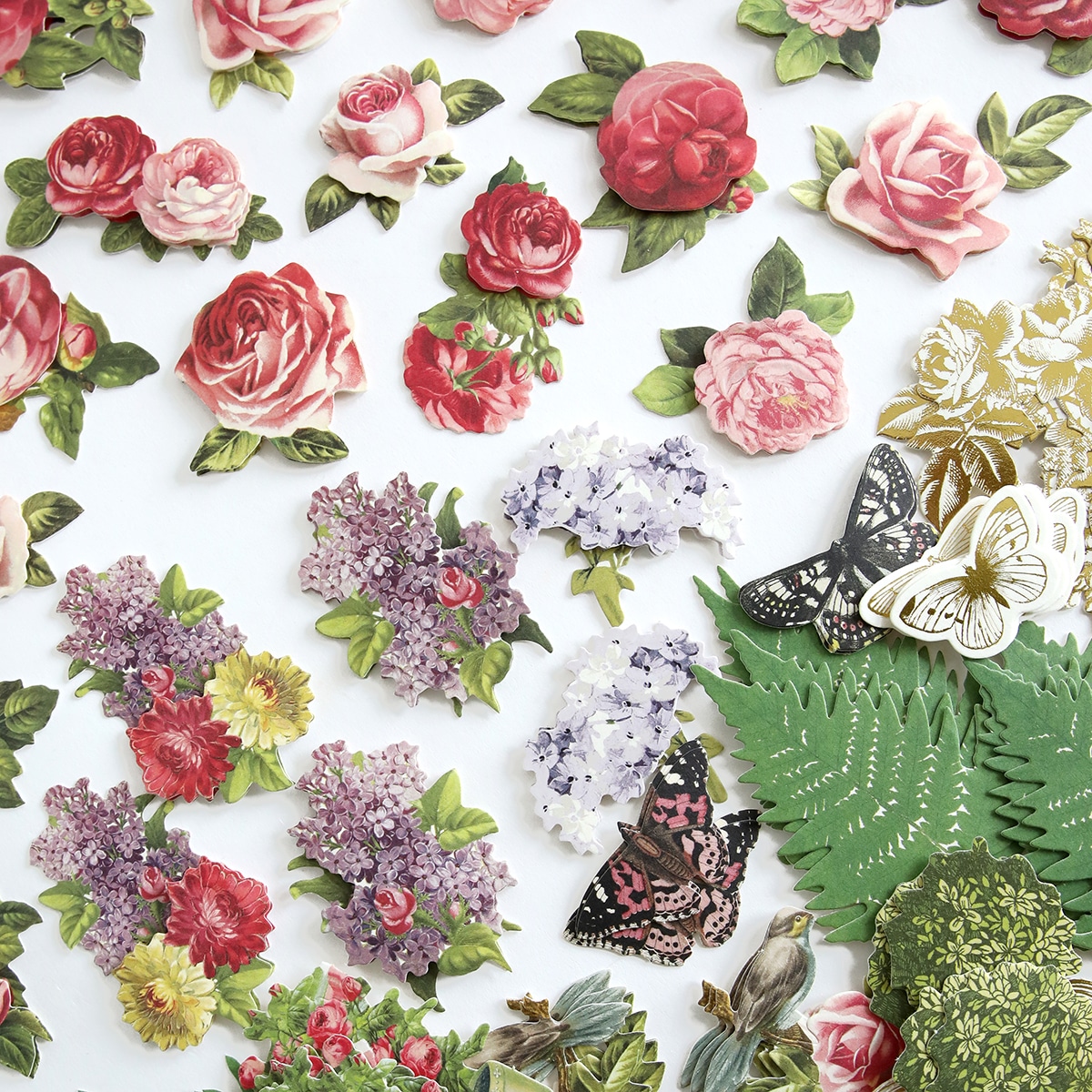 A variety of paper flowers and leaves are arranged on a white surface.