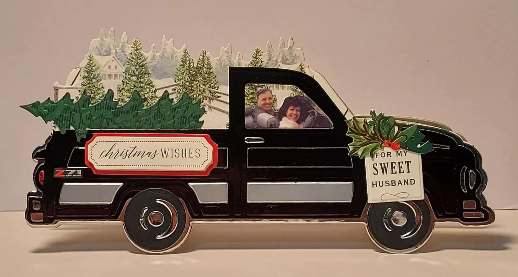 A christmas card with a christmas tree in the back of a truck.